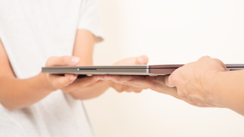 Один человек передает ноутбук другому человеку