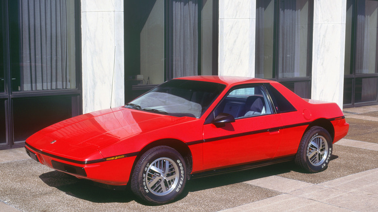 Красный Pontiac Fiero 1983 года выпуска, припаркованный перед зданием.