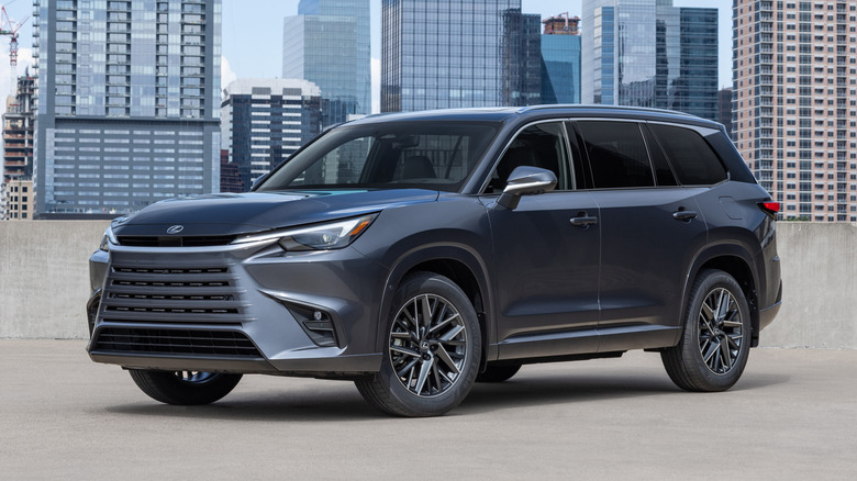 Черный Lexus TX 2026 года припаркован на фоне городского пейзажа.