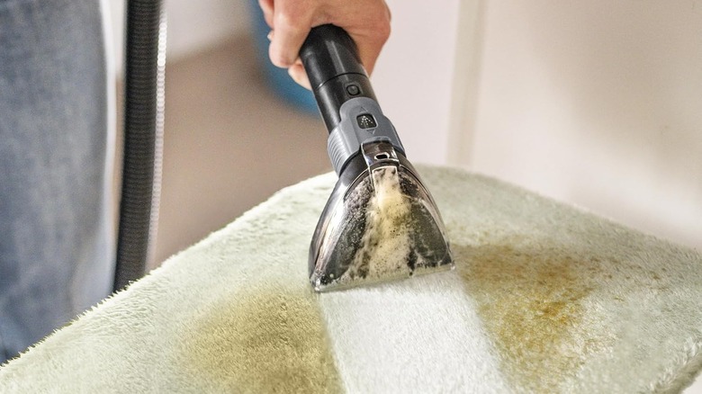 Портативный очиститель обивки высасывает грязь с зеленого коврика для ванной