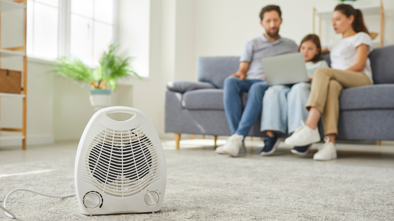 Небольшой электрический обогреватель на полу рядом с людьми, сидящими на диване.
