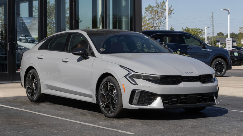 Угловая фотография передней и боковой части серого Kia K5 2025 года выпуска.