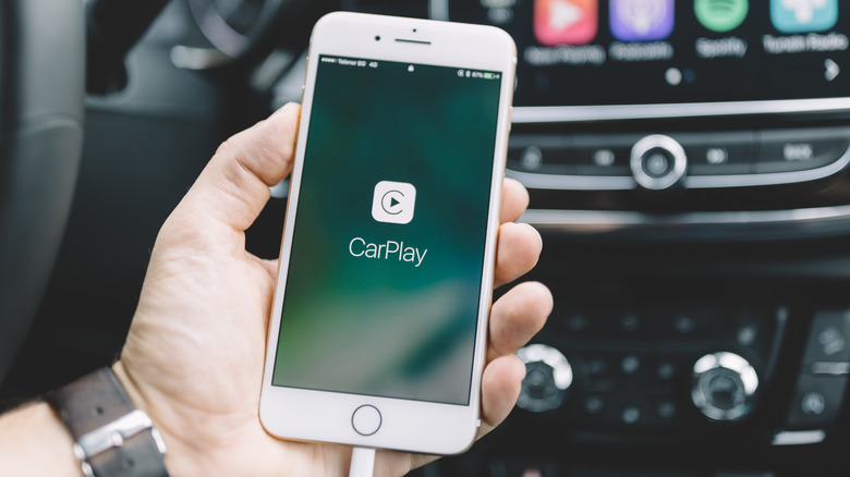 Человек выбирает значок карты на информационно-развлекательном экране CarPlay левым указательным пальцем