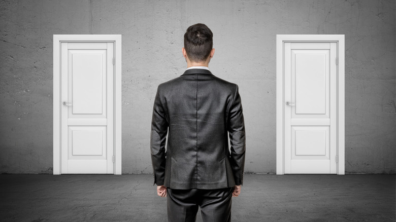 Мужчина в костюме стоит перед двумя одинаковыми белыми дверями.