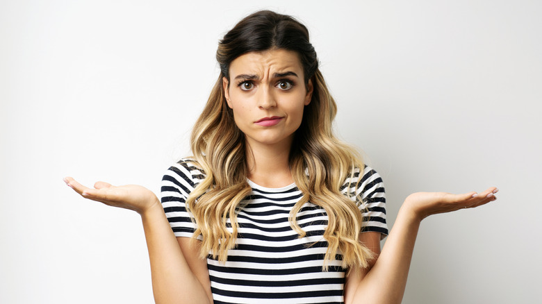 Женщина с длинными светлыми волосами, полосатой рубашкой и озадаченным выражением лица.