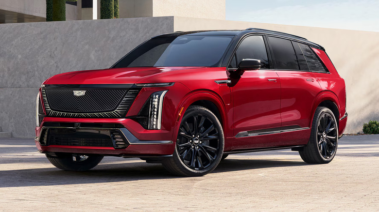 вид спереди слева на красный внедорожник Cadillac Vistiq, припаркованный на городском тротуаре со стеной и зданием позади