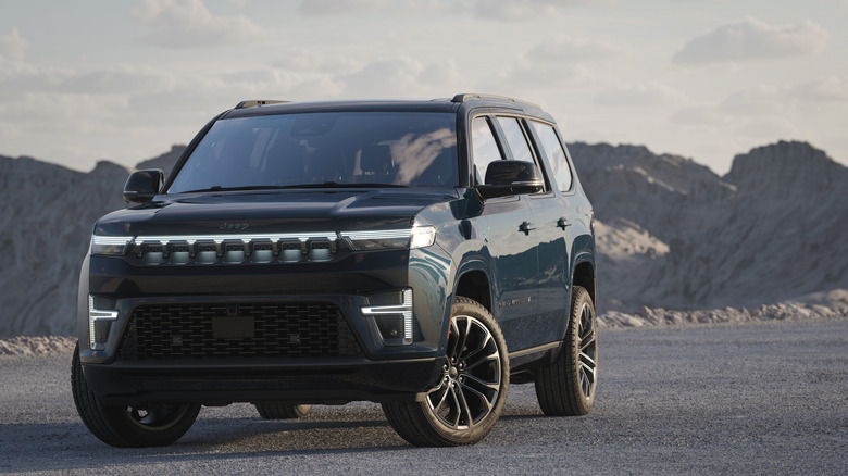 Вид спереди темно-синего Jeep Grand Wagoneer на гравийной площадке в горах