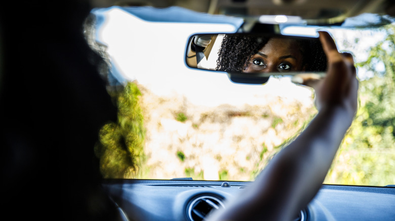 Водитель регулирует зеркало заднего вида.