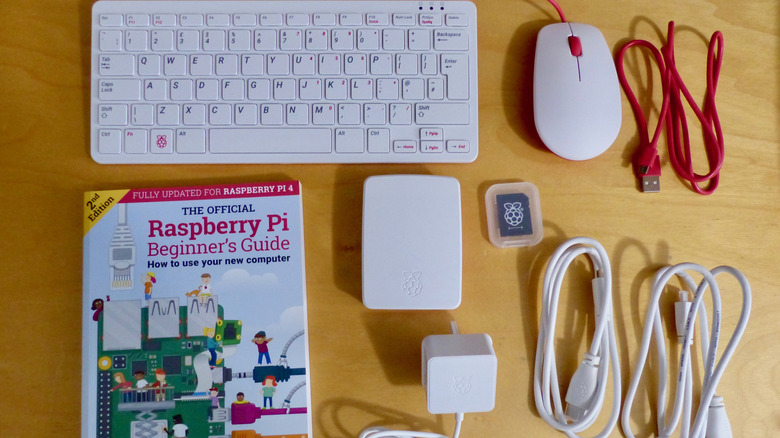 На столе лежит комплект Raspberry Pi с кучей шнуров, мышью, клавиатурой и книгой.