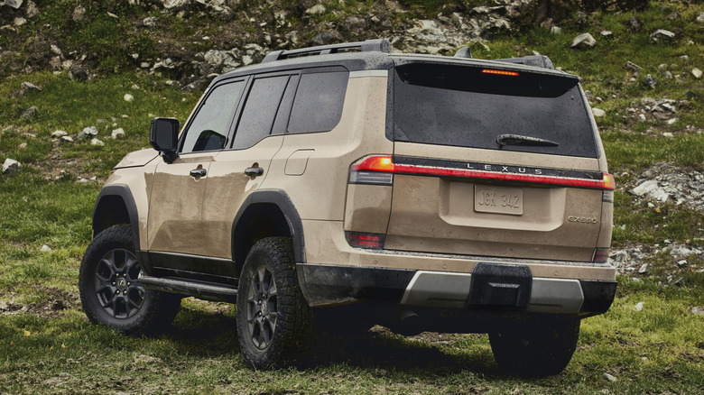 Вид сзади на 3/4 золотого Lexus GX 550 на склоне холма с камнями и травой