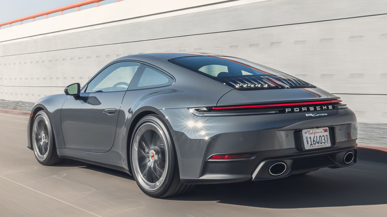 Вид сзади на 3/4 серого Porsche 911 Carrera Coupe на дороге со стеной на заднем плане