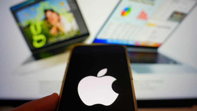 Изображение iPhone с логотипом Apple на экране и изображение MacBook на заднем плане.