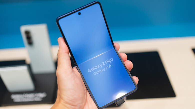 Крупный план руки, держащей телефон Samsung Galaxy Z Flip7 возле витрины магазина.