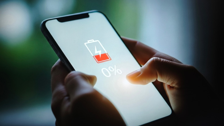 Человек, держащий смартфон с индикатором на экране, показывающим разряженную батарею