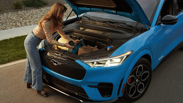 Женщина хватает вещи из открытого багажника синего Ford Mustang Mach-E GT.