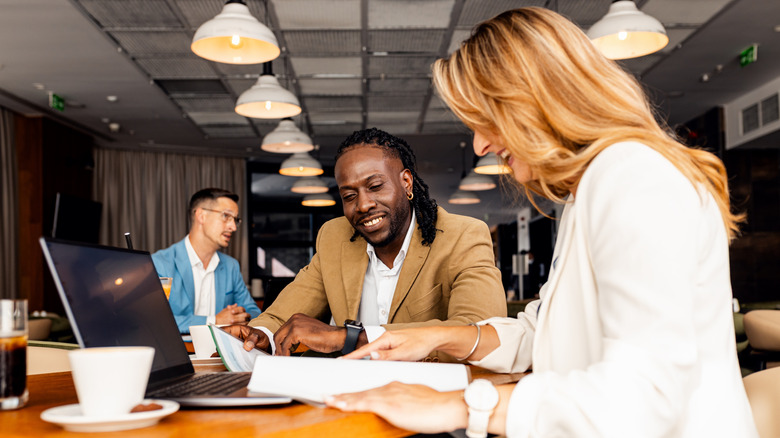 коллеги говорят о работе, используя ноутбук в современной кофейне