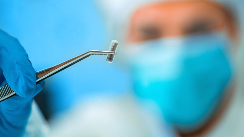 Доктор держит RFID-имплантат пинцетом