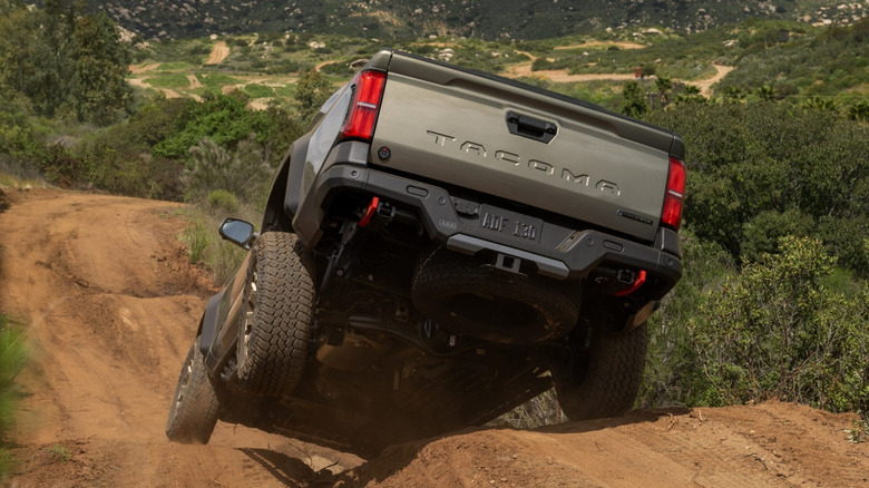 Вид сзади на 3/4 бронзовой Toyota Tacoma на холмистой грунтовой дороге по бездорожью