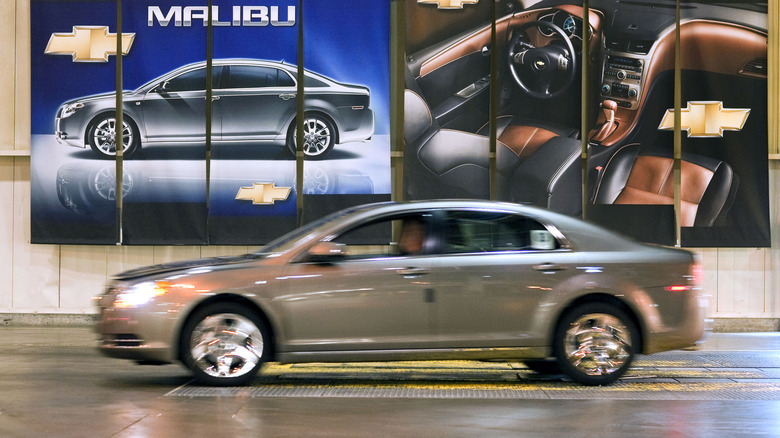 Вид сбоку в профиль серого Chevrolet Malibu 2010 года выпуска, размытый в движении.