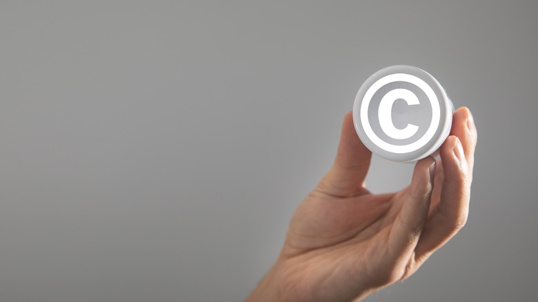 Рука, держащая логотип авторских прав на сером фоне