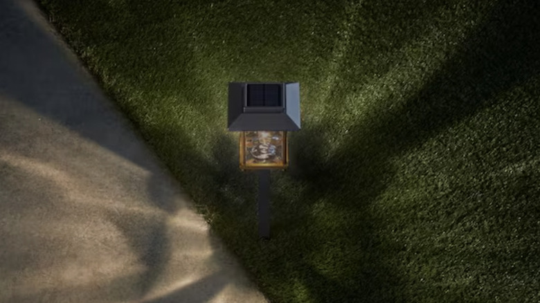 Единственный солнечный фонарь Hampton Bay Parkwood Bronze освещает тротуар и искусственный газон.