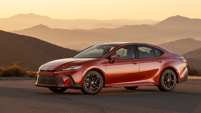 Красная Toyota Camry SE 2026 года припаркована на закате перед горами.