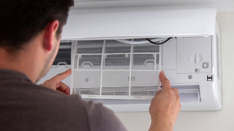 Мужчина устанавливает чистый фильтр в кондиционере