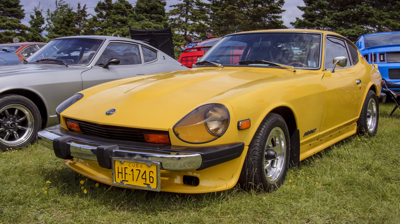 Желтый Datsun 280Z 1970-х годов, припаркованный на лужайке, вокруг него стояли другие машины.