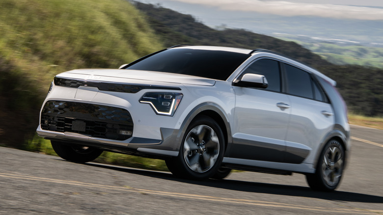 Вид спереди на 3/4 белого Kia Niro EV с серыми деталями на холмистой дороге