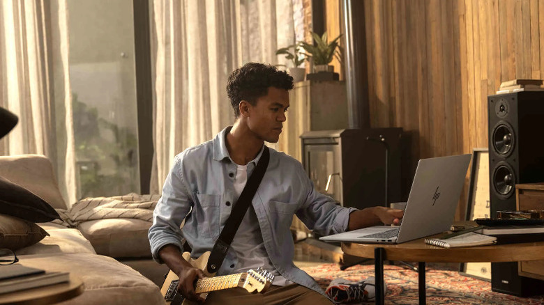 Человек одной рукой пользуется HP OmniBook 7, а в другой держит гитару.