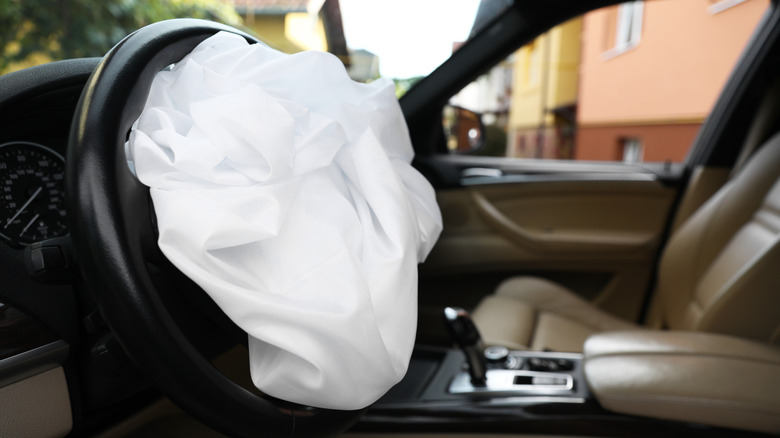 Сработавшая подушка безопасности внутри автомобиля, похожего на BMW с кремовыми кожаными сиденьями.