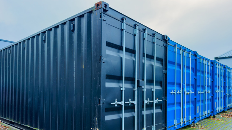 Ряд ярких транспортных контейнеров возвышается на гравийной площадке.