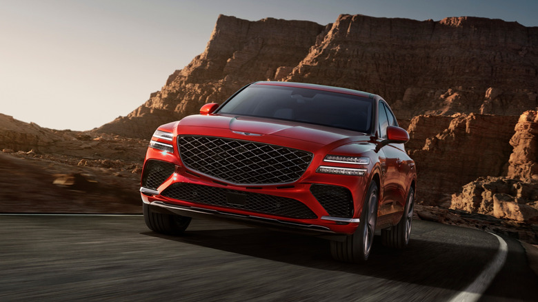 Красный Genesis GV80 Coupe едет по сельской пустынной дороге.