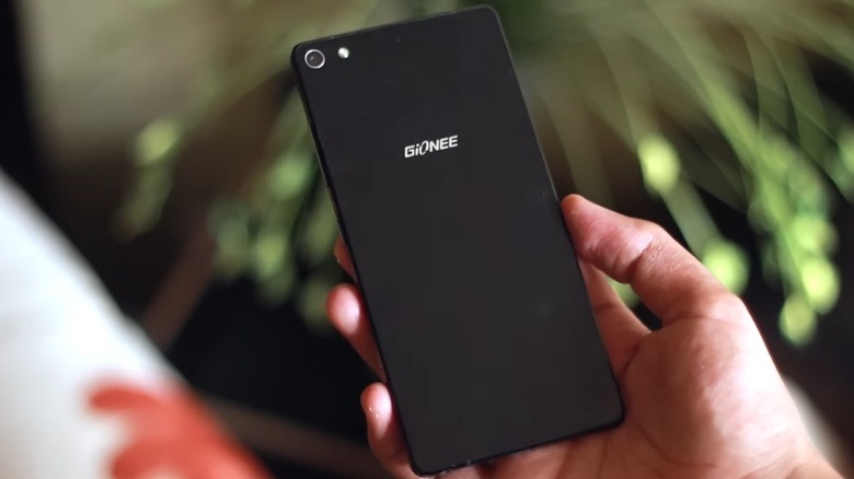 Рука держит Gionee Elife S7 перед расфокусированным растением