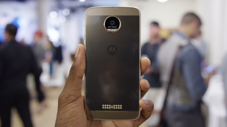 Рука держит Moto Z на фоне расфокусированных людей