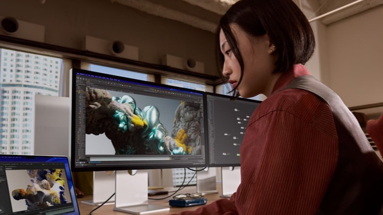 Женщина смотрит на ноутбук рядом с Apple Studio Display