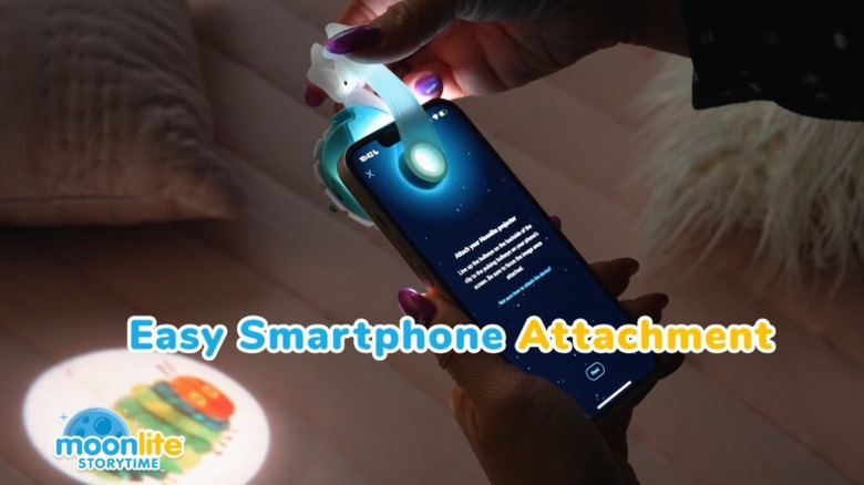 Женщина прикрепляет к своему iPhone проектор Moonlight Storytime.