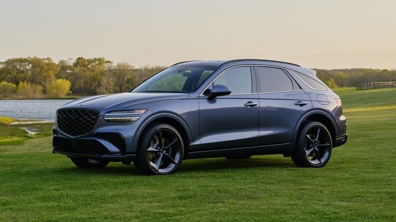 Голубовато-серый Genesis GV70 в поле, вид спереди на 3/4, солнечный день