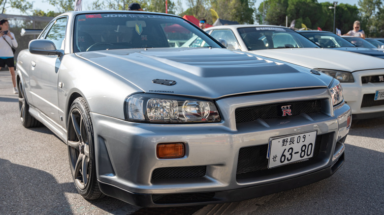 Серый Nissan Skyline R34 припаркован рядом с другими автомобилями JDM на автосалоне JDM.