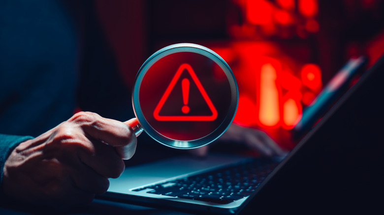 Человек, держащий увеличительное стекло с цифровым символом оповещения над ноутбуком