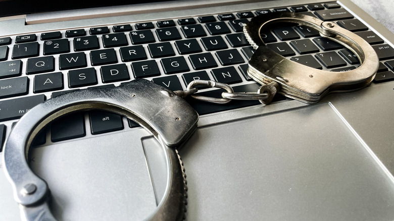Крупный план серебряного ноутбука с металлическими наручниками, лежащего на черной клавиатуре