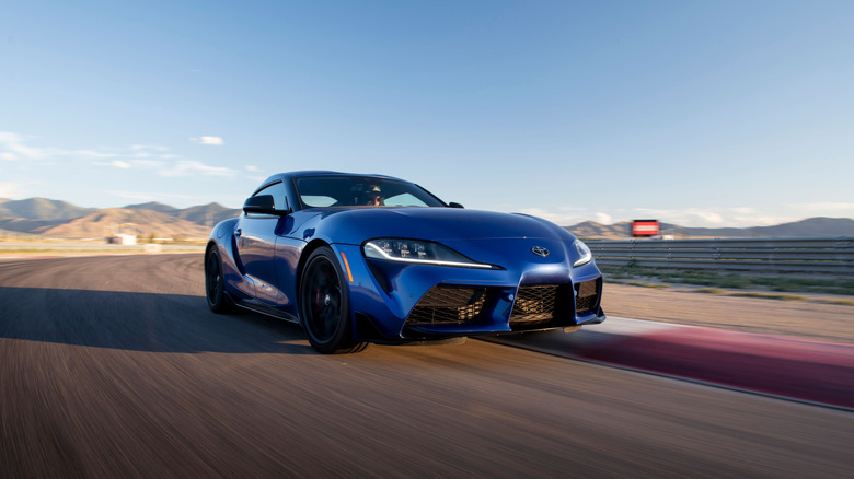 Toyota GR Supra 2026 года за рулем на гоночной трассе, вид спереди справа в 3/4