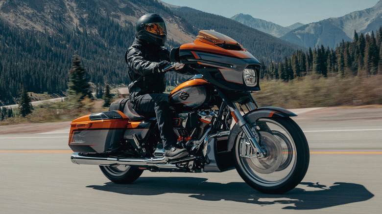 Человек едет на Harley-Davidson Street Glide по сельской дороге на фоне гор.
