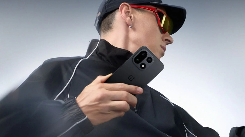 Человек, одетый в черное, позирует с OnePlus 15.