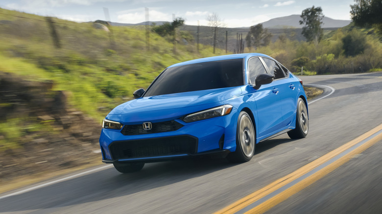 Синий Honda Civic Hybrid 2026 года в движении по горной дороге, вид спереди 3/4