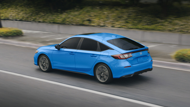 Синий Honda Civic Hybrid 2026 года в движении по городской дороге, вид сзади в 3/4