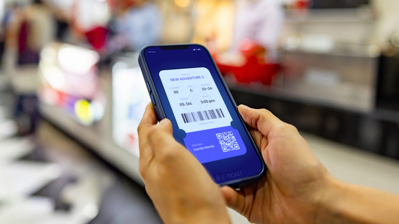 Крупный план билета в кино, отображаемого на смартфоне в чьих-то руках возле торговой палатки в кинотеатре.