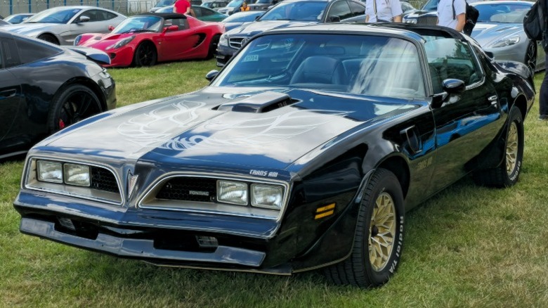 Черно-золотой Pontiac Firebird Trans Am, припаркованный на траве на автосалоне.