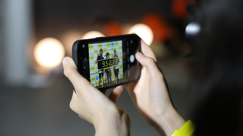 Руки держат iPhone и фотографируют трёх финишировавших марафонцев