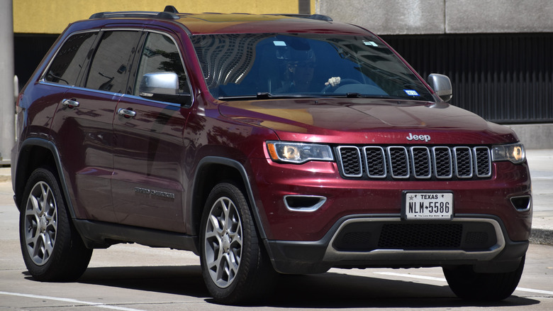 Вид спереди на красный Jeep Grand Cherokee, едущий по дороге.